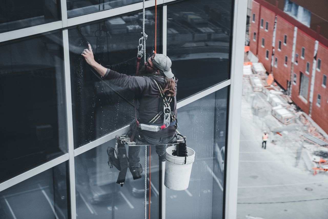 services-02 A worker cleaning skyscraper windows with a harness in an urban setting.