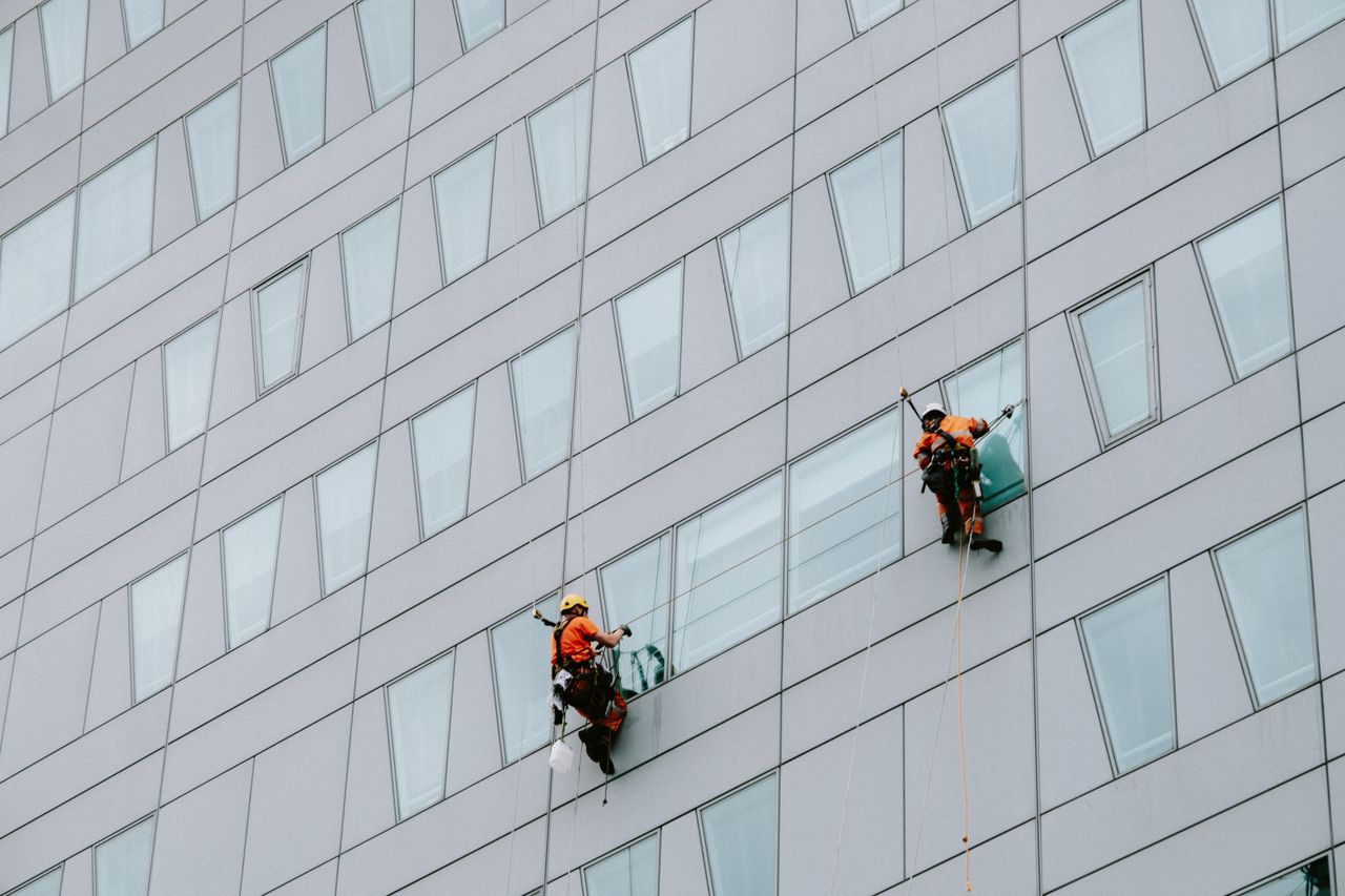 services-02 High-rise window washers in safety gear cleaning a skyscraper facade.